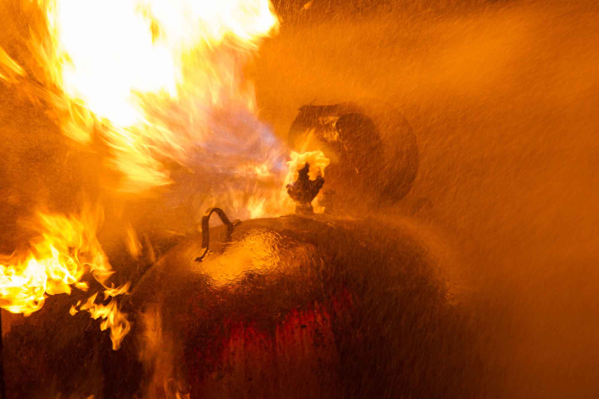 A large fire is partially drenched by a fire hose